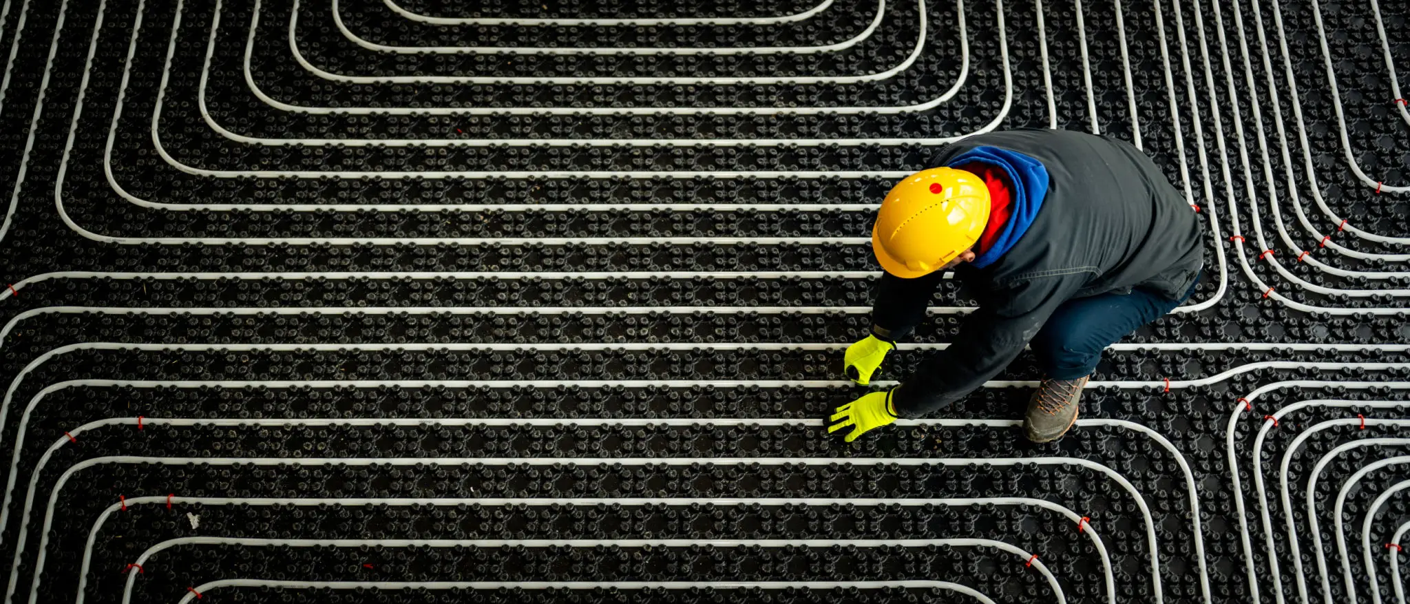 Worker installing underfloor heating pipes in a patterned layout.