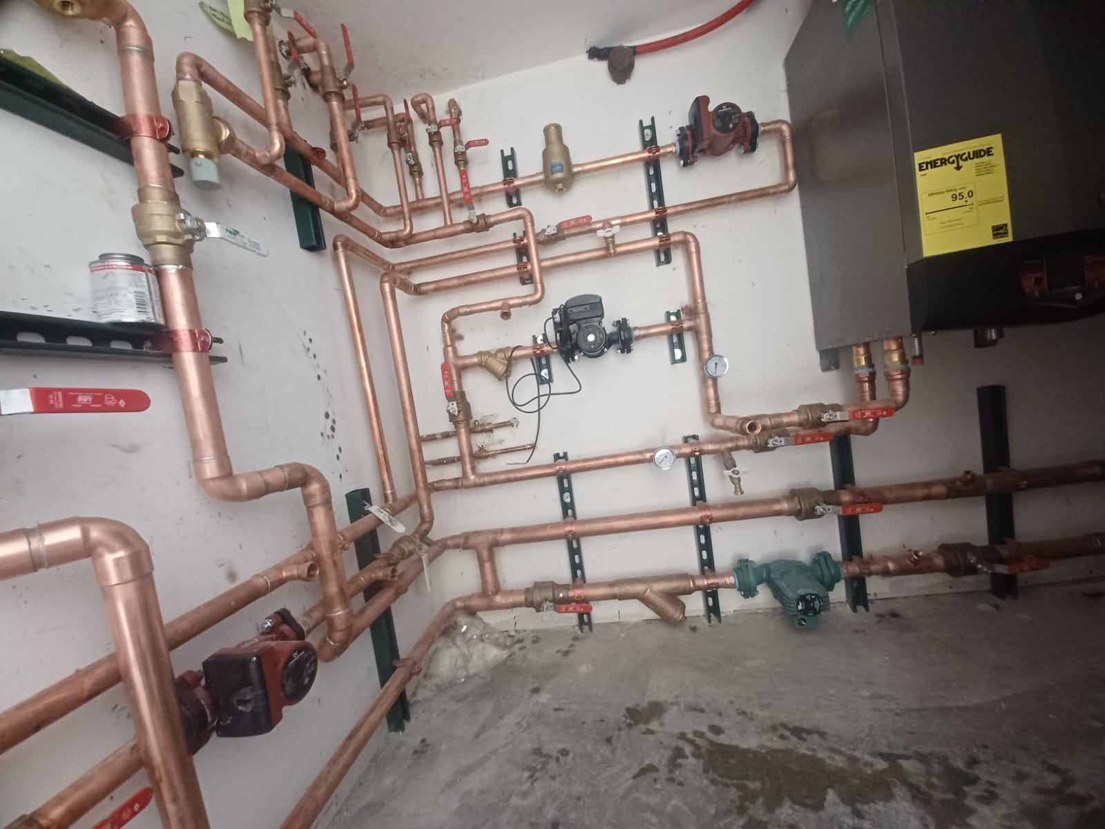 Complex network of copper pipes and valves on a wall in an industrial setting.