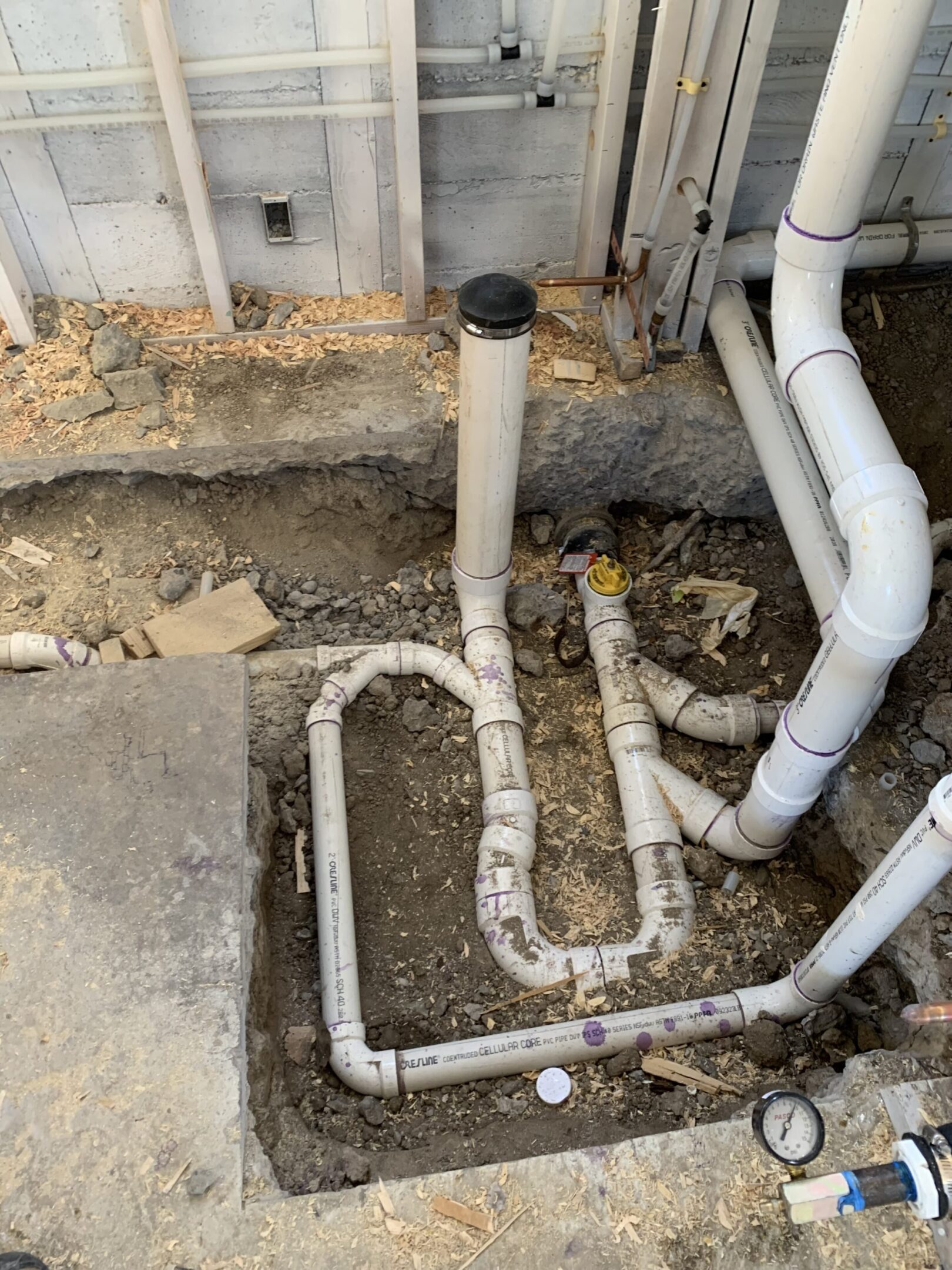 Exposed plumbing pipes in a basement floor under repair.